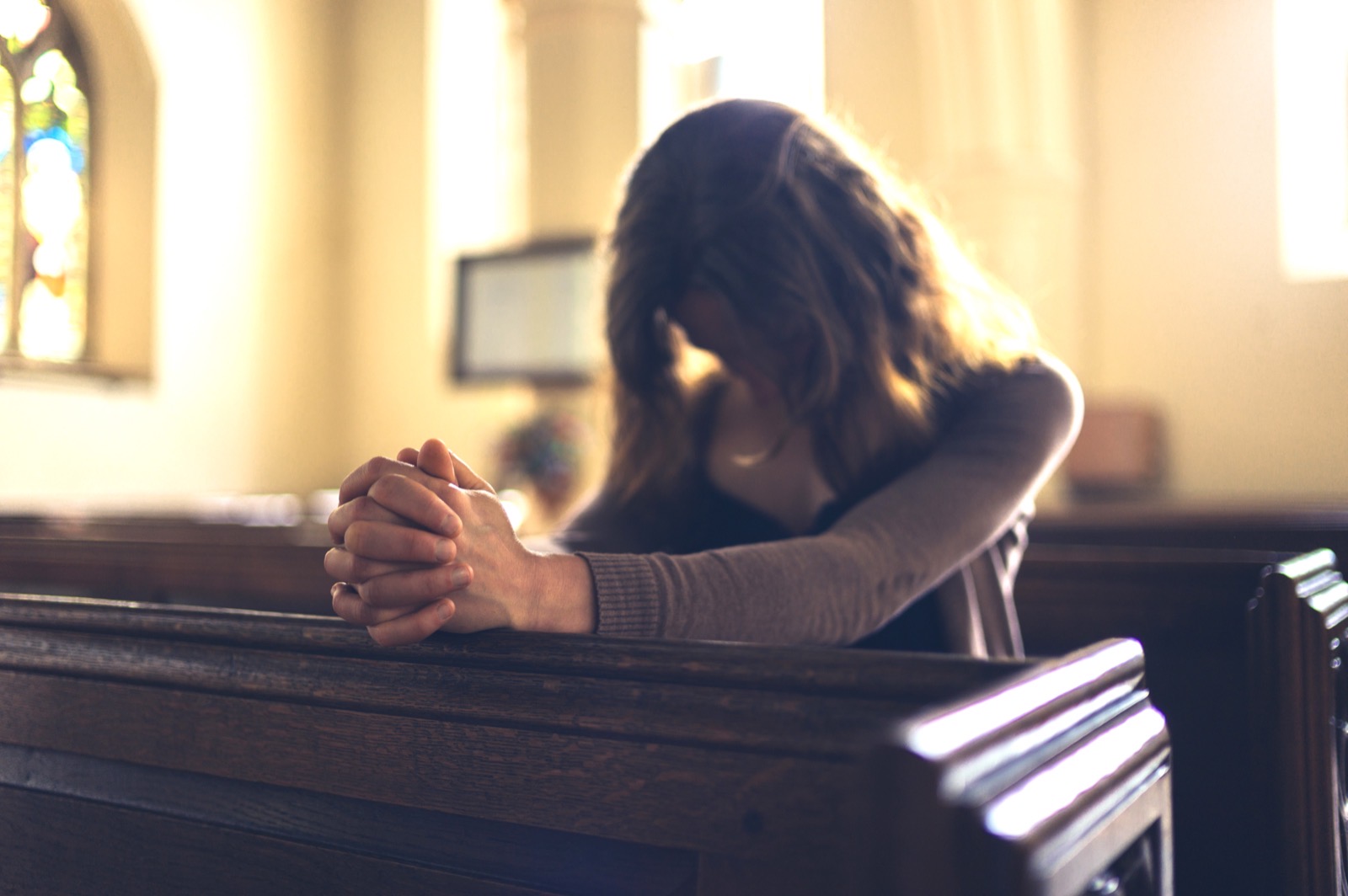 A woman prays with folded hands in a church pew